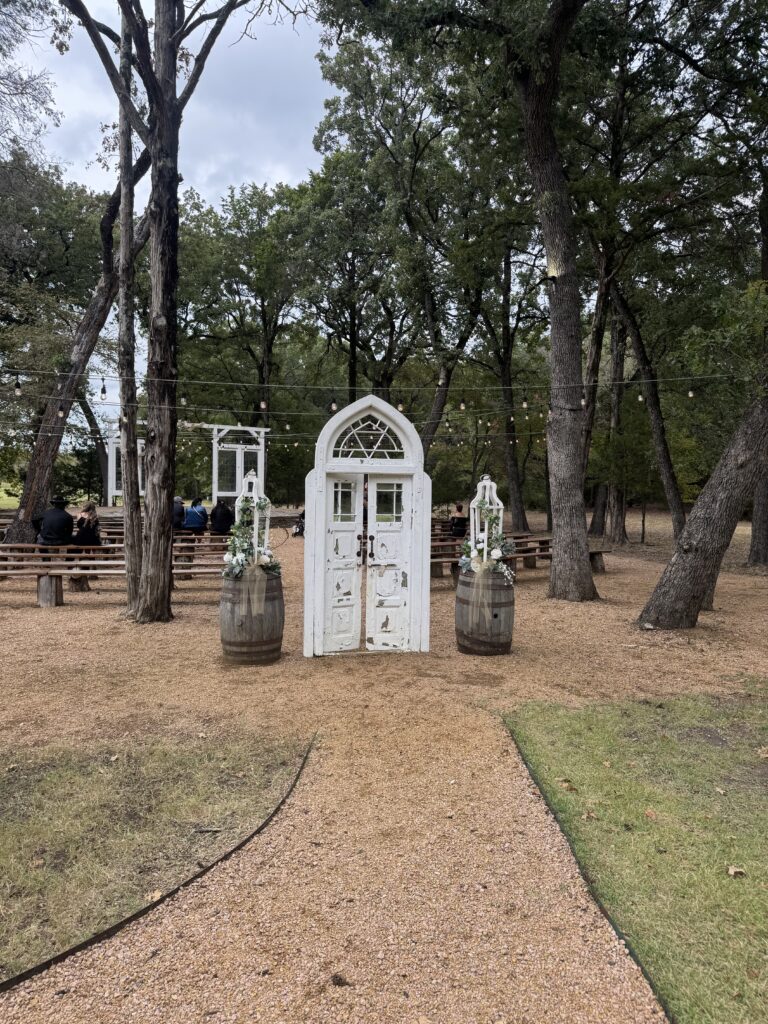 Outdoor wedding at the establishment barn with rustic white doors, string lights overhead, and wooden benches