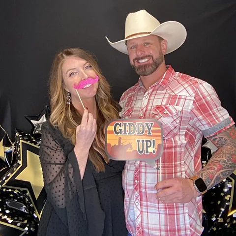 Couple holding a Giddy Up sign and pink mustache prop at the photo booth