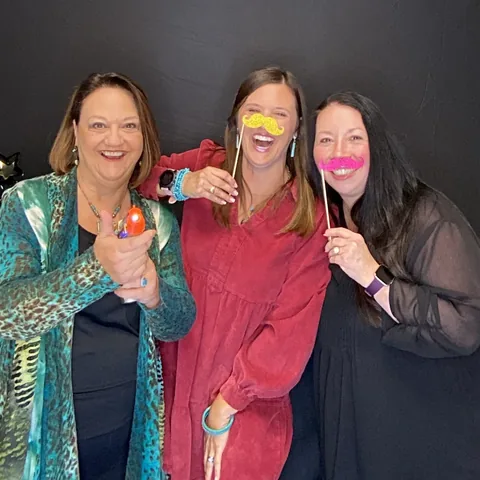 Three friends laughing with mustache props at the photo booth