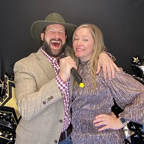 Laughing couple with a cowboy hat and microphone prop at the photo booth