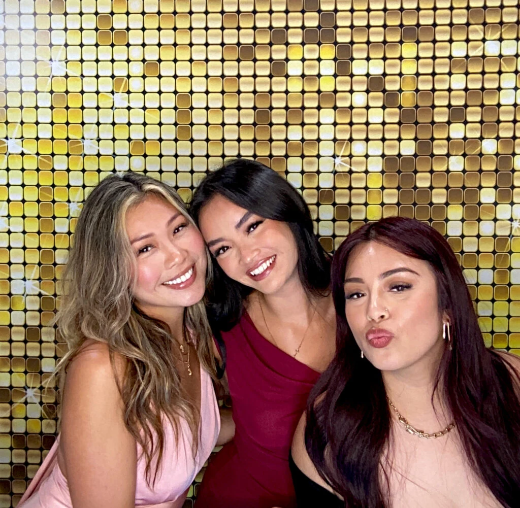 Three guests posing in front of a gold sequin backdrop