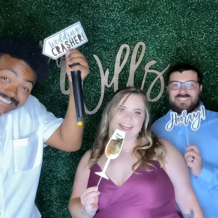Three photo booth guests posing with props in front of a green backdrop